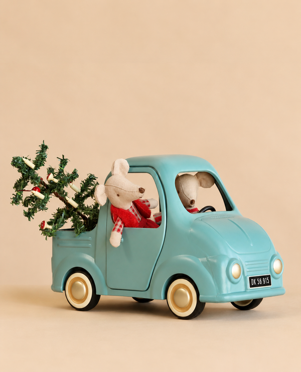 Two Maileg Christmas twin mice ride in a blue toy pickup truck from the Maileg Christmas Truck Set, which carries a small decorated Christmas tree in the truck bed.