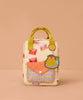 The Sticky Lemon Backpack Small - Special Edition - Snail Mail is a small beige kids backpack featuring red and pink geometric shapes, a yellow handle, orange plaid front pocket, green fruit-shaped keychain, and waterproof lining from recycled PET bottles.