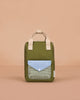 The Sticky Lemon Backpack Small - Envelope - Tickling Grass is a kids’ olive green backpack with beige handles, a blue flap pocket, and a checkered front pocket made from recycled PET bottles, shown on a plain peach background.