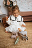 A young girl in a white dress with black trim plays on a carpeted floor with toy animals, including a zebra and the Handmade Wooden Hippo. In the background, a wicker basket and a flower vase enhance the charming scene with child-safe paint accents.