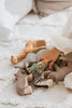 A child's hand reaches for toy animals like a giraffe, elephant, zebra, and rhinoceros on a cream blanket, including a Handmade Wooden Hippo finished with child-safe pastel paint.