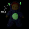An Olli Ella Dinky Dinkum Doll - Miles Monster glow-in-the-dark plush toy with green horns and belly, wearing a fuzzy purple suit with a rainbow emblem, next to text that reads “Glows in the dark!”.