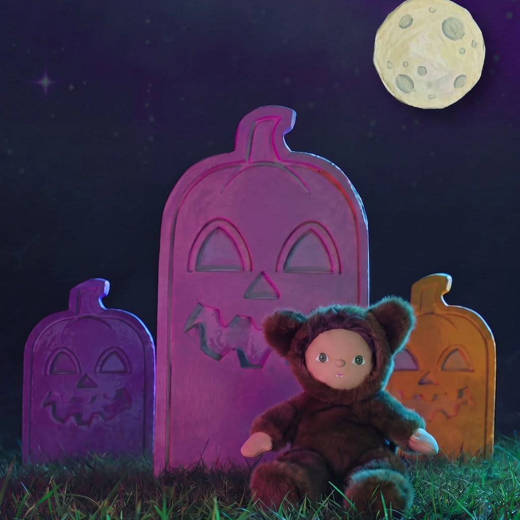 An Olli Ella Dinky Dinkum Doll - Wesley Werewolf sits in the grass in front of three carved jack-o’-lanterns under a full moon.