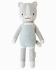 Cuddle + Kind Dylan the Kitten is a soft, hand-knit gray cat doll with white accents, a smiling face, and light blue striped overalls, featuring a simple and cute design. Shown on a white background.