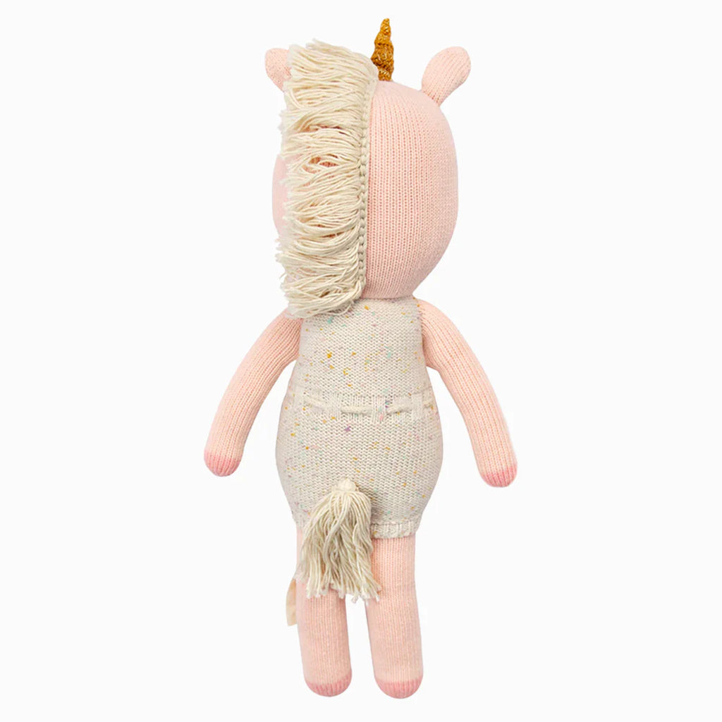 Cuddle + Kind Ella the Unicorn is a stuffed pink unicorn toy with a gold horn, cream mane and tail, and a light speckled outfit, shown from the back on a white background.