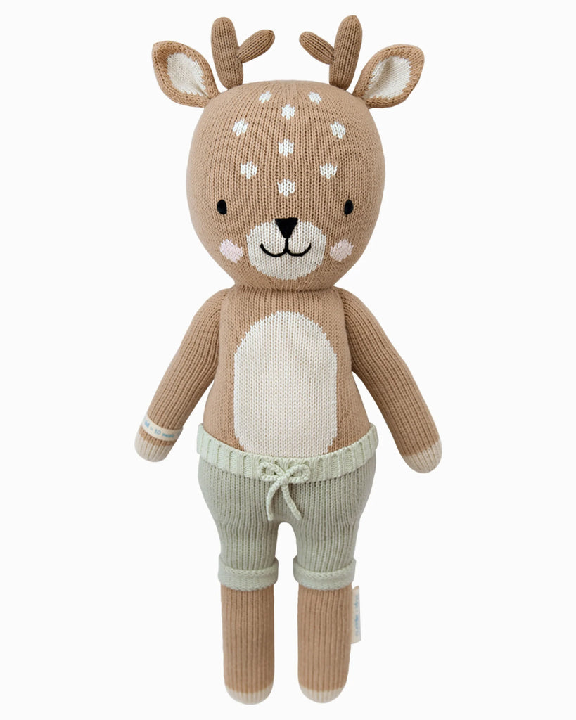 Cuddle + Kind Elliott the Fawn is a sustainable, fair trade, hand-knit plush doll featuring antlers, a light brown body with white spots, and light green drawstring pants, shown upright against a white background.