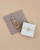 The Maileg Bunny Rattle Set - Cream Peach includes a plush bunny toy and a charming rattle on a small blue-beige blanket, alongside a floral gift box with "Bunny Baby" text, making it an ideal gift against the soft, neutral beige background.