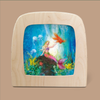 Introducing "Silhouette Only - Underwater World for Toverlux Lamp": This enchanting artwork captures a mermaid perched on a rock in an underwater realm, extending her arm towards a large orange fish. The lively scene is enriched with mystical silhouettes of sea plants and jellyfish. It comes beautifully framed in a decorative wooden frame with curved edges, showcased against a neutral backdrop.
