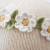 A close-up of Cuddle + Kind Hannah the Bunny's cream-colored premium cotton yarn fabric, adorned with crocheted white flowers featuring yellow centers and green leaves.