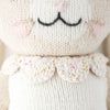Close-up of Cuddle + Kind Hannah the Bunny, a hand-knit doll made from premium cotton yarn, with embroidered black mouth, pink nose, whiskers, and a scalloped collar adorned with pastel specks.