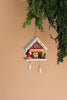 The Christian Ulbricht Ornament - Santa with Red Cuckoo, showcasing a charming small Santa figure adorned with holiday decorations, dangles from a branch against a beige backdrop. Crafted in Germany, this exquisite piece is not a toy and lends an authentic touch to your seasonal decor.