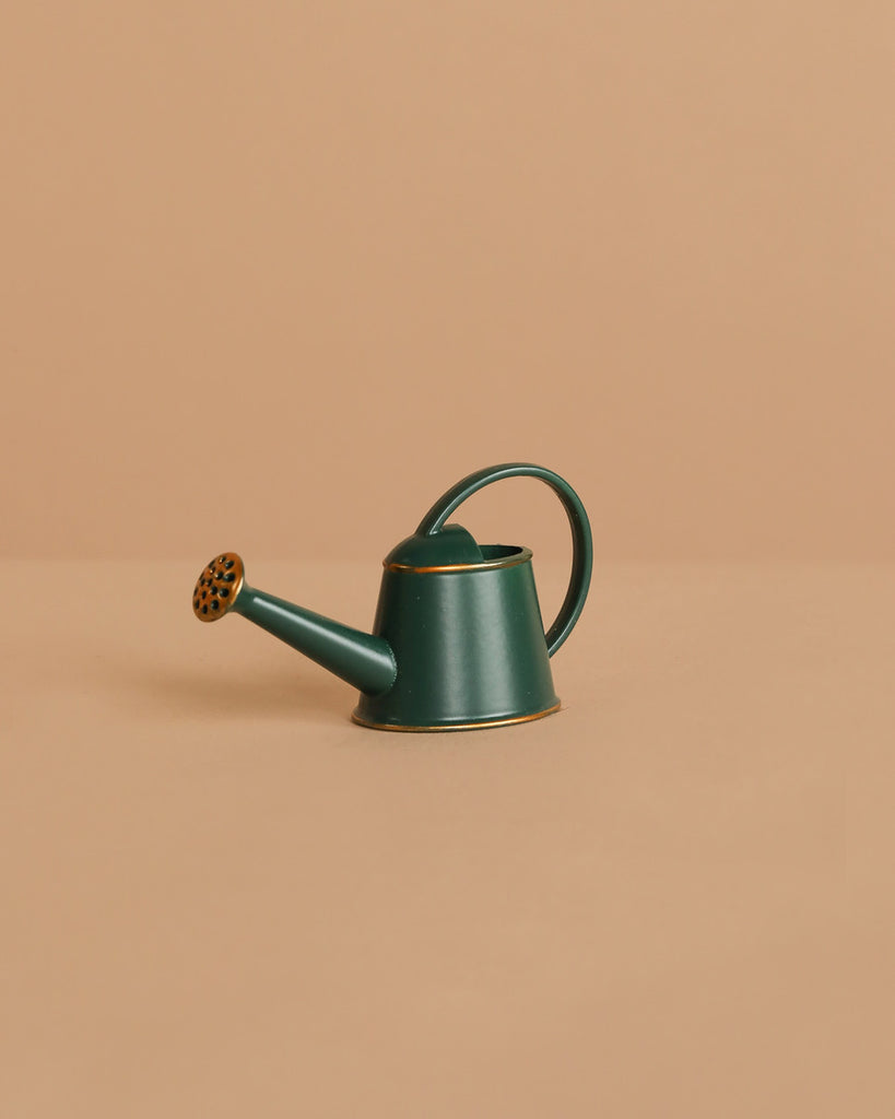 The Maileg Little Green Thumb Garden Set features a small green metal watering can with a rounded handle and spout, perfect for a Maileg Mouse or to pair with a Maileg Flower Pot on a beige surface.