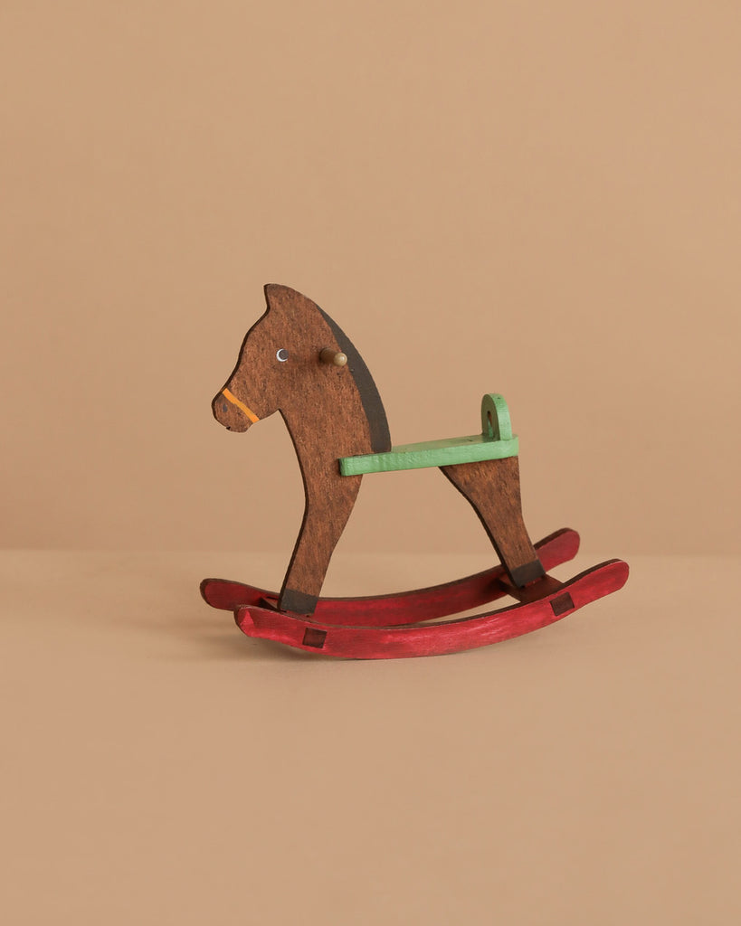 The Maileg Nursery Set includes a small rocking horse toy featuring a brown body, green handle, and red rockers, set against a plain beige background.