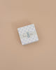 Consider gifting the Maileg Bunny Rattle Set - Mint. This charming small square box features a floral pattern, gray ribbon with a playful blue bunny, and "bunny baby" text on a beige background, perfectly sized to hold soft cotton cloths or the sweet bunny rattle.