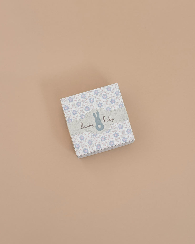 Consider gifting the Maileg Bunny Rattle Set - Mint. This charming small square box features a floral pattern, gray ribbon with a playful blue bunny, and "bunny baby" text on a beige background, perfectly sized to hold soft cotton cloths or the sweet bunny rattle.