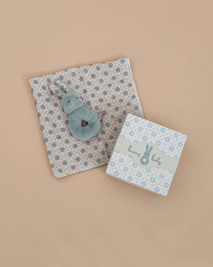 The Maileg Bunny Rattle Set - Mint includes a rabbit-eared soft toy on a floral cotton cloth with a decorative box, making an ideal gift set against a neutral beige backdrop.