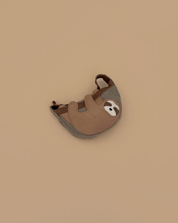 The Donsje Leather Talei Bumbag Purse - Sloth is a small, brown and gray kids bag shaped like a smiling sloth, featuring an adjustable strap, shown on a plain beige background.
