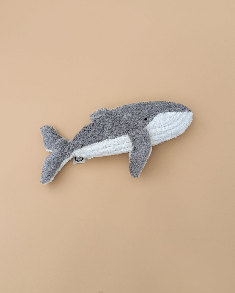 The Senger Naturwelt Cuddly Animal - Whale, crafted from organic cotton in gray and white, sits on a beige background and doubles as a cozy handmade warming pillow.