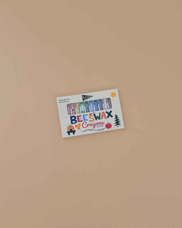 A box of 12 Beeswax Crayons – Non-Toxic with colorful sticks visible through playful, brightly illustrated packaging sits on a plain beige surface.