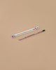 A Strawberry Plantable Pencil – Eco-Friendly with a green tip rests beside a white box adorned with red strawberries and leaves, both crafted from sustainable materials, set on a light brown background.