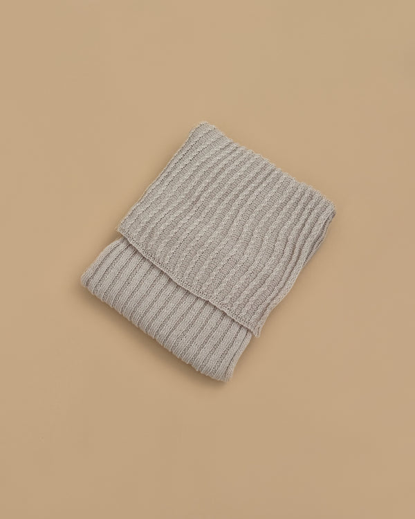 The Maileg Baby Blanket, in a light gray ribbed knit, is folded and displayed on a plain beige background, exuding the warmth and coziness of a comforting blanket.