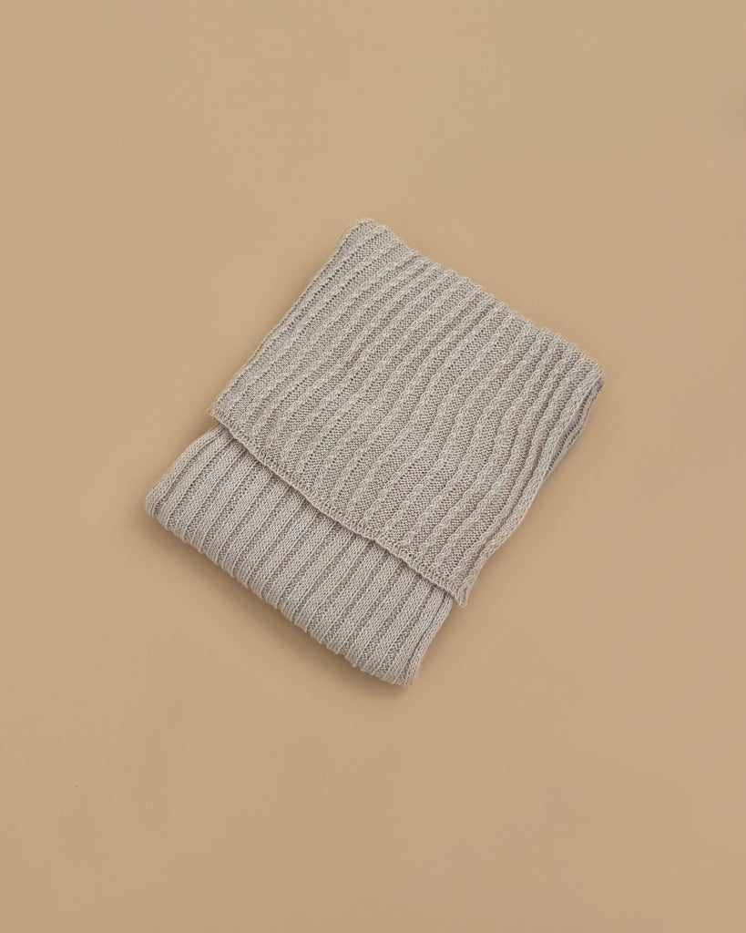 The Maileg Baby Blanket, in a light gray ribbed knit, is folded and displayed on a plain beige background, exuding the warmth and coziness of a comforting blanket.