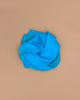 A vibrant turquoise Sarah's Silks Solid Color Playsilk is gently folded atop a neutral beige surface, forming soft curves for a simple, elegant look—ideal for open-ended play.