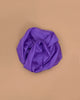 A purple Sarah's Silks Solid Color Playsilk rests crumpled on a flat, light brown surface, viewed from above—capturing the creative spirit of open-ended play.