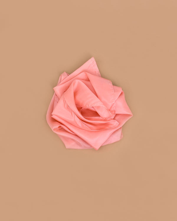 A peach heavy pure silk fabric, folded and arranged like a rose, sits against a plain light brown background—perfect for open-ended play with Sarah's Silks Heavy Playsilk Large - Peach.
