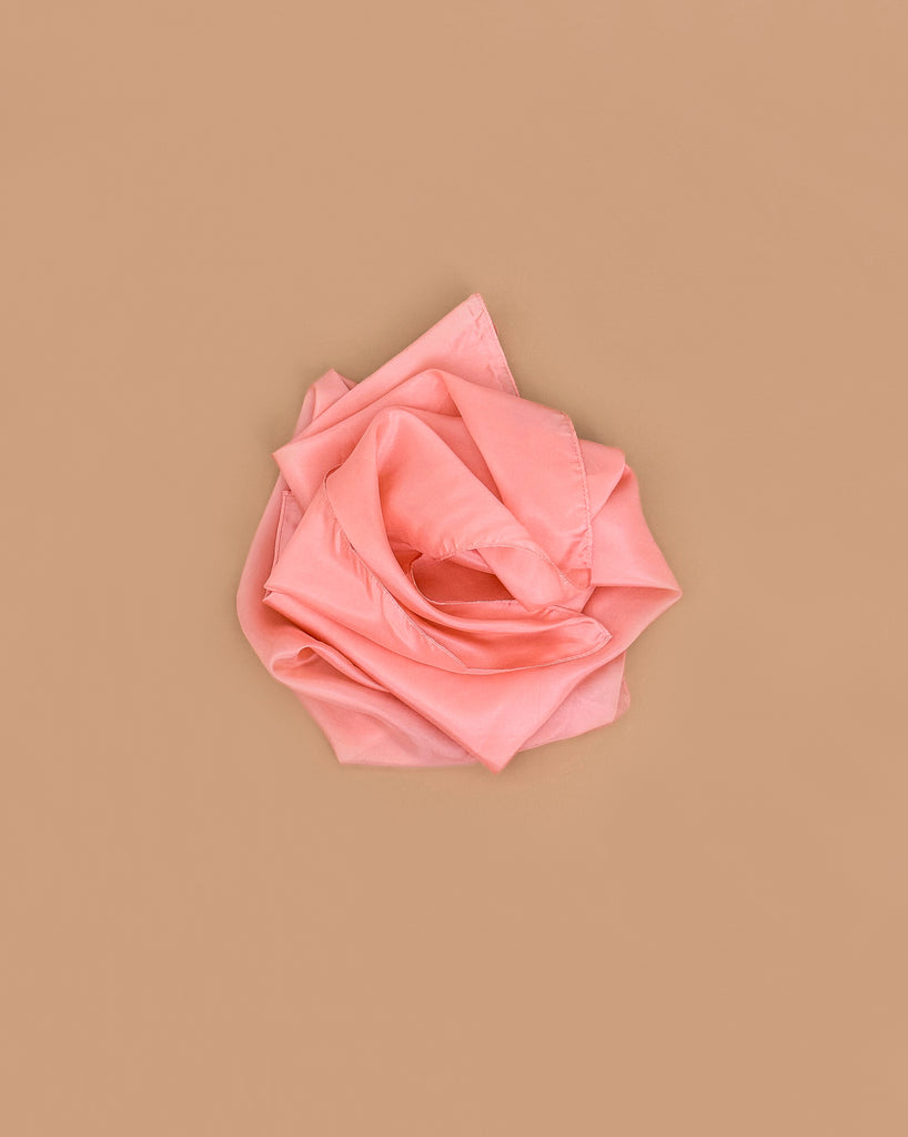 A peach heavy pure silk fabric, folded and arranged like a rose, sits against a plain light brown background—perfect for open-ended play with Sarah's Silks Heavy Playsilk Large - Peach.