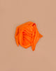 Sarah's Silks Solid Color Playsilk in Orange, loosely folded on a light brown background, inspires imaginative, open-ended play and brings elegance to sensory play activities.