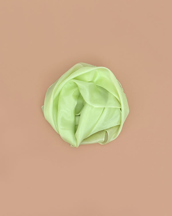 Sarah's Silks Solid Color Playsilk - Lime, a silky light green scarf, is rolled in a circle on a plain light brown background—ideal for open-ended and sensory play.