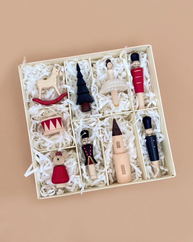 The Sabo Concept Christmas Ornaments set includes nine hand-painted wooden decorations—ballerina, rocking horse, drum, Christmas tree, nutcracker, soldiers, church, and more—arranged in a box with compartments and white shredded paper.