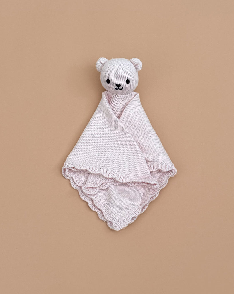 The Cuddle + Kind Organic Cotton Baby Bear Lovey (Blush) is a soft, light pink lovey with a plush bear head and simple embroidered face, pictured on a solid beige background.