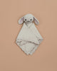 The Cuddle + Kind Organic Cotton Baby Bunny Lovey (Oatmeal), featuring floppy ears and embroidered facial details, is hand-knit and lies on a plain beige background.