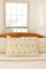 A neatly made bed features the Organic Cotton Layered Gauze Pillowcase - Teddy in beige, paired with white bedding and set against a wooden headboard, with sheer curtains framing a bright window behind.