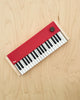 The Loog Piano is a compact, minimalist digital piano with velocity-sensitive black and white keys, a red panel, a single black knob, and light wooden sides, shown on a light wood surface.