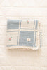 The Organic Cotton Patchwork Baby Blanket - Spring Bloom features a blue and white checkered pattern, small embroidered flowers, and crochet trim, shown folded on a white quilted surface.