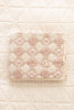 The Organic Cotton Baby Patchwork Blanket - Pink Bows (ships in one week), featuring a diamond quilted pattern and lace trim, is folded on a textured, cream-colored surface.