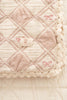 A close-up of the Organic Cotton Baby Patchwork Blanket - Pink Bows, featuring soft quilted cotton in beige and light pink with a diamond pattern, lace trim, and delicate details—perfect as a baby blanket. Ships in one week.