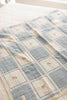 The Organic Cotton Patchwork Baby Blanket - Spring Bloom features soft, quilted organic cotton in blue and cream squares with embroidered pink flowers, displayed atop a lightly patterned bedspread.
