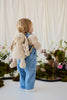 A toddler in denim overalls stands with their back to the camera, wearing an adjustable hazelnut Snuggle Bunnies - Penelope Backpack.