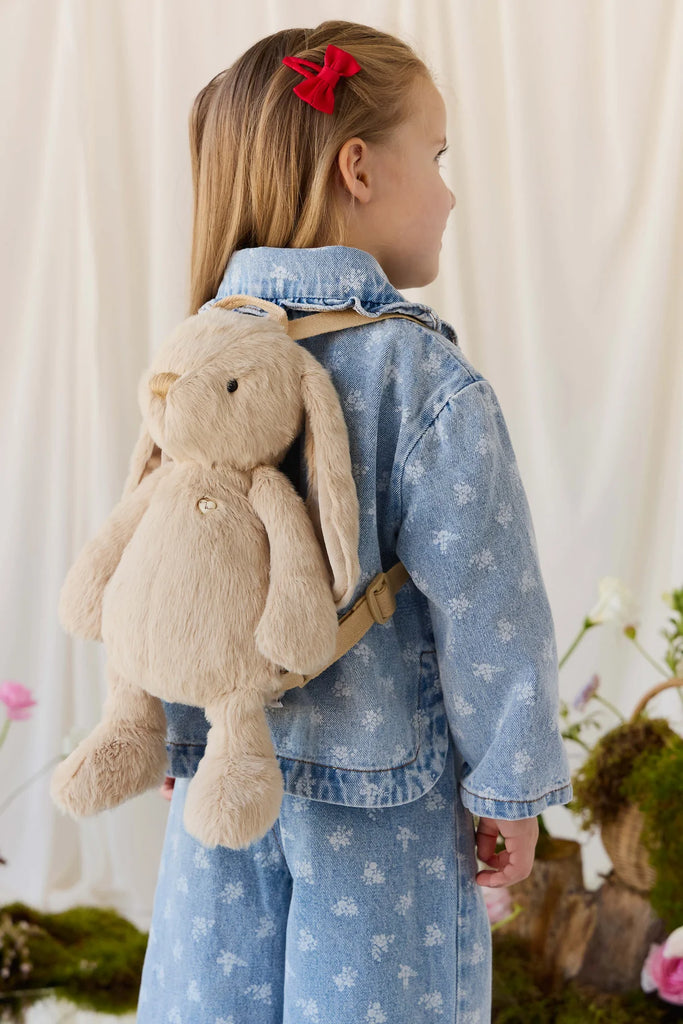 A child wearing a Snuggle Bunnies - Penelope Backpack - Hazelnut, a light brown plush bunny backpack with adjustable straps.
