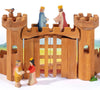 The Ostheimer Round Tower is a beautifully handcrafted wooden castle featuring two round towers connected by a central gate. The set includes four wooden figures: two positioned at the base of the castle engaging in playful interaction and two stationed atop the towers facing each other. A small bird figure delicately perches on the left tower, all set against a peaceful landscape designed to inspire imaginative play.