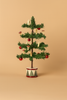 A Maileg Cozy Christmas Corner with Little Sister featuring a small artificial tree in a painted drum base, decorated with red ball ornaments, miniature candles, and mushroom ornaments.