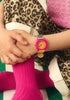 A person in leopard print pants, a pink top, and bright pink socks sits cross-legged, hands on their knee, wearing a Mini Kyomo Watch - Disco with Japanese movement on their wrist.