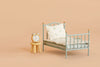 A small blue metal bed with floral bedding and a pillow sits next to the Maileg Stool Set, Mouse - Mint/Light Yellow, which holds a silver alarm clock, all set against a light beige background. The bed’s vintage paint finish adds extra charm to this cozy scene.