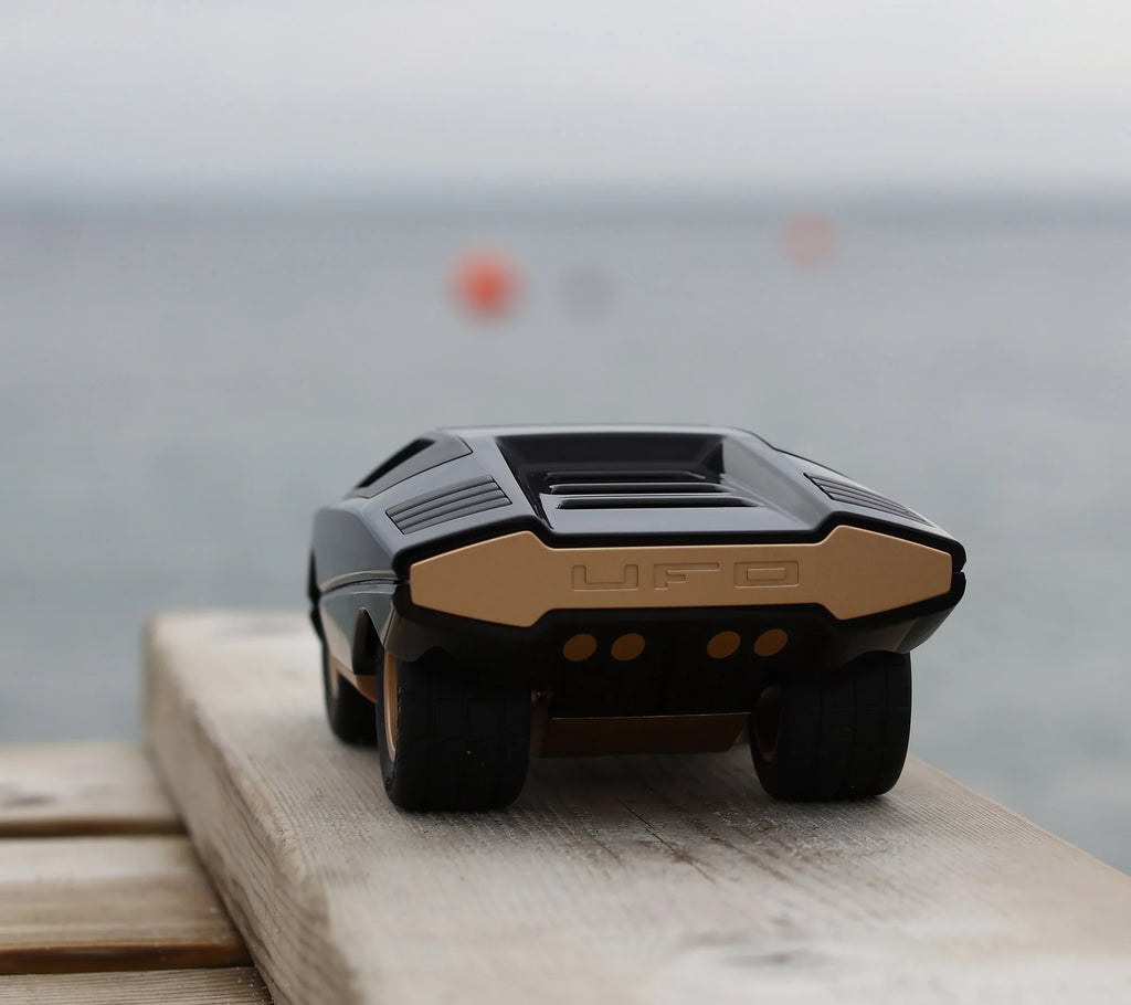 The Playforeer UFO Cannone Car in Black, inspired by 70’s concept cars, captures the spirit of vintage super cars in miniature form on a wood surface.