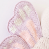 Close-up of a knitted butterfly wing in pastel colors. The wing, crafted from soft Peruvian cotton yarn, features a heart-shaped lilac border with a pattern of white and pink stitches on a light purple background. This delicate piece is perfect for any collection of Cuddle + Kind Baby Butterfly or other keepsakes.