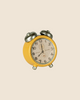 A small yellow vintage alarm clock with two bells on top, displaying 12:00, sits beside the charming Maileg Living Room Set, featuring a miniature fireplace against a plain beige background, creating a cozy scene reminiscent of Maileg mouse furniture and dollhouse accessories.